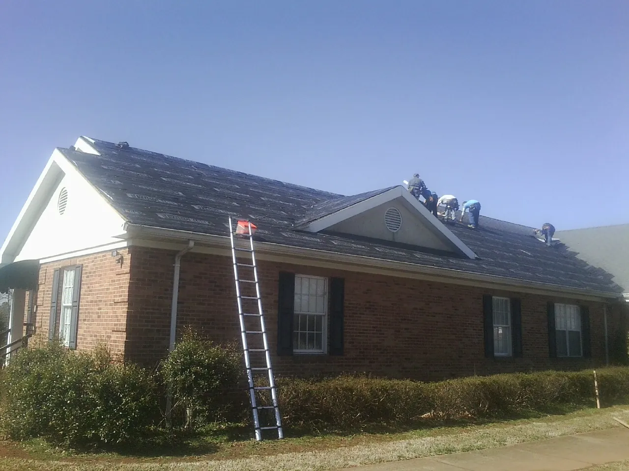 Crew tearing shingles off a brick ranch roof with a ladder set — Metal Roof Repair work by our crew in Cape Neddick