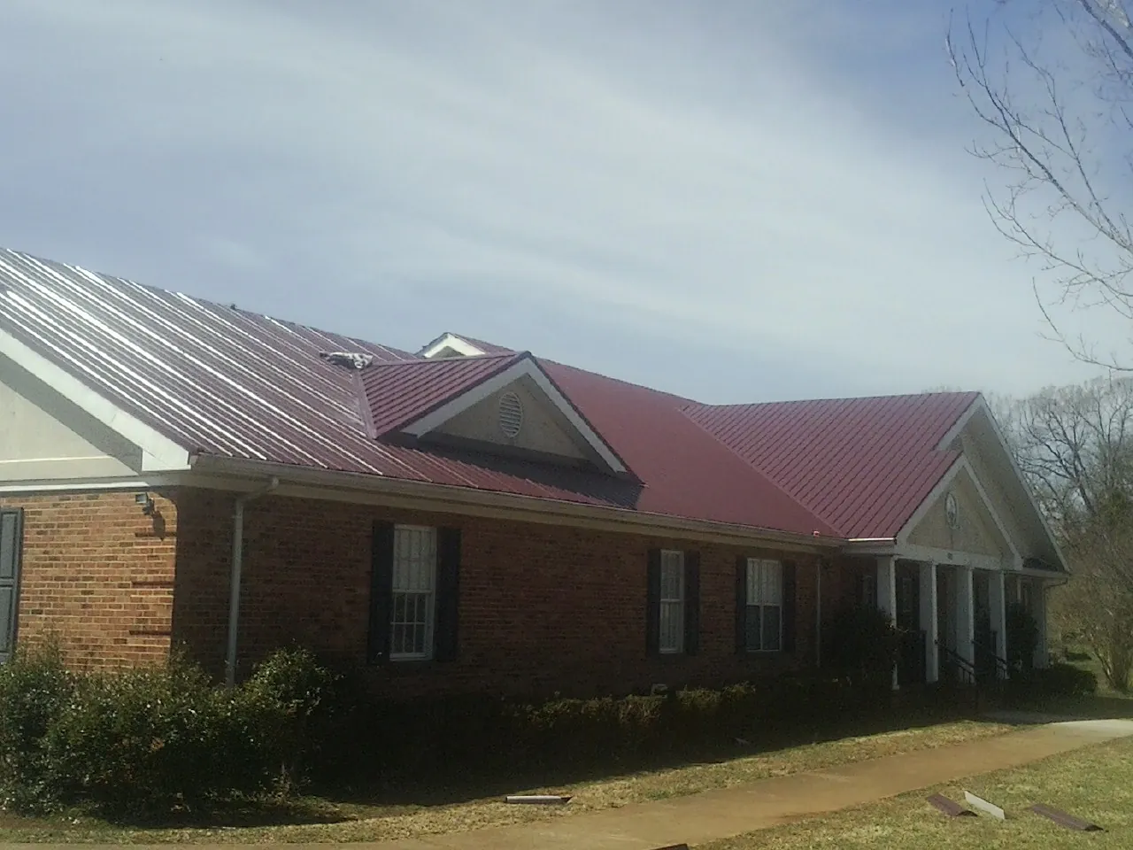 Red metal roof with gabled entries on a long brick building, from a Hail Damage Roof Repair job in Cape Neddick