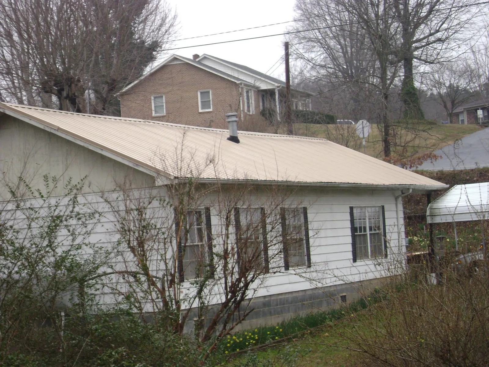 Tan metal roof on a white sided house set into a hillside — Commercial Roofing by Roofing Brothers in Cape Neddick